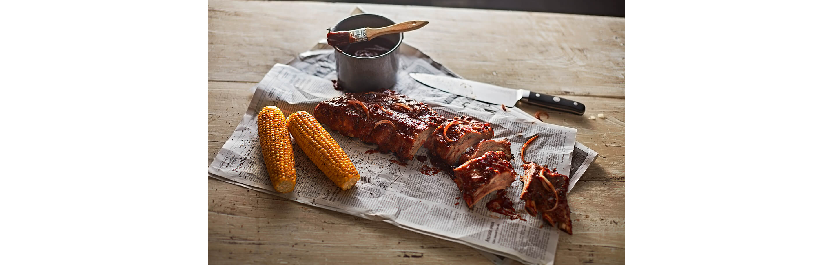 A sliced rack of barbeque ribs resting on newspaper.