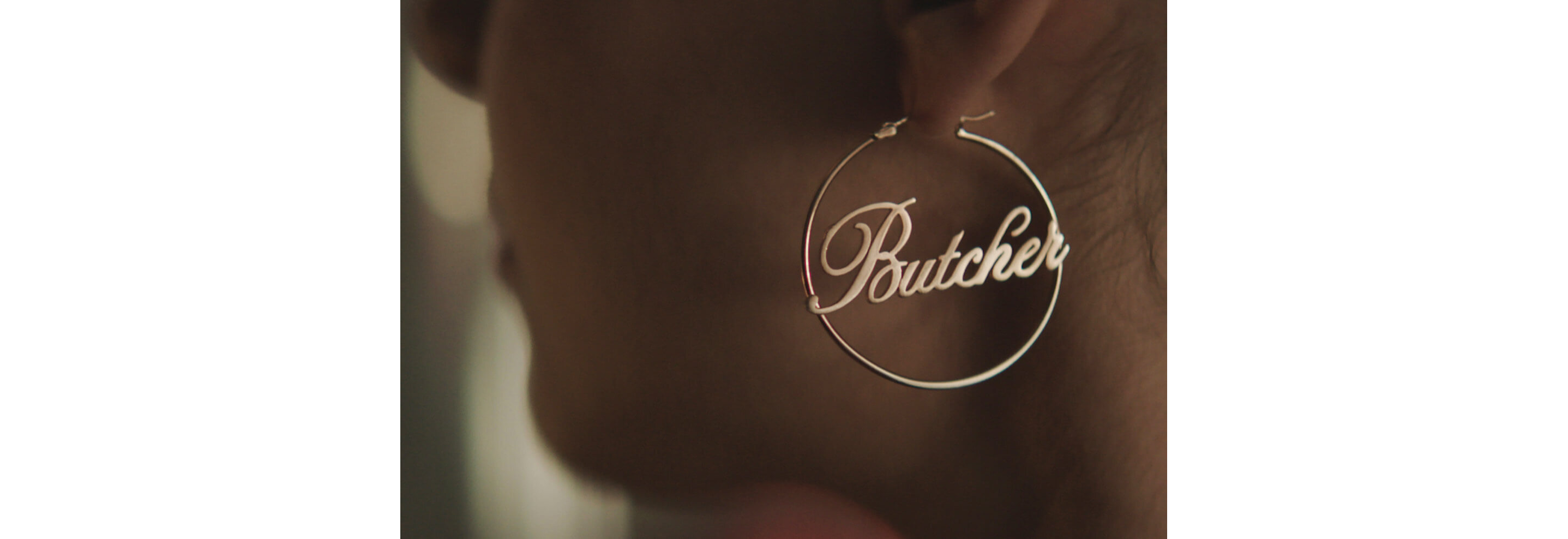 A golden hoop earring with a cursive Butcher in center.