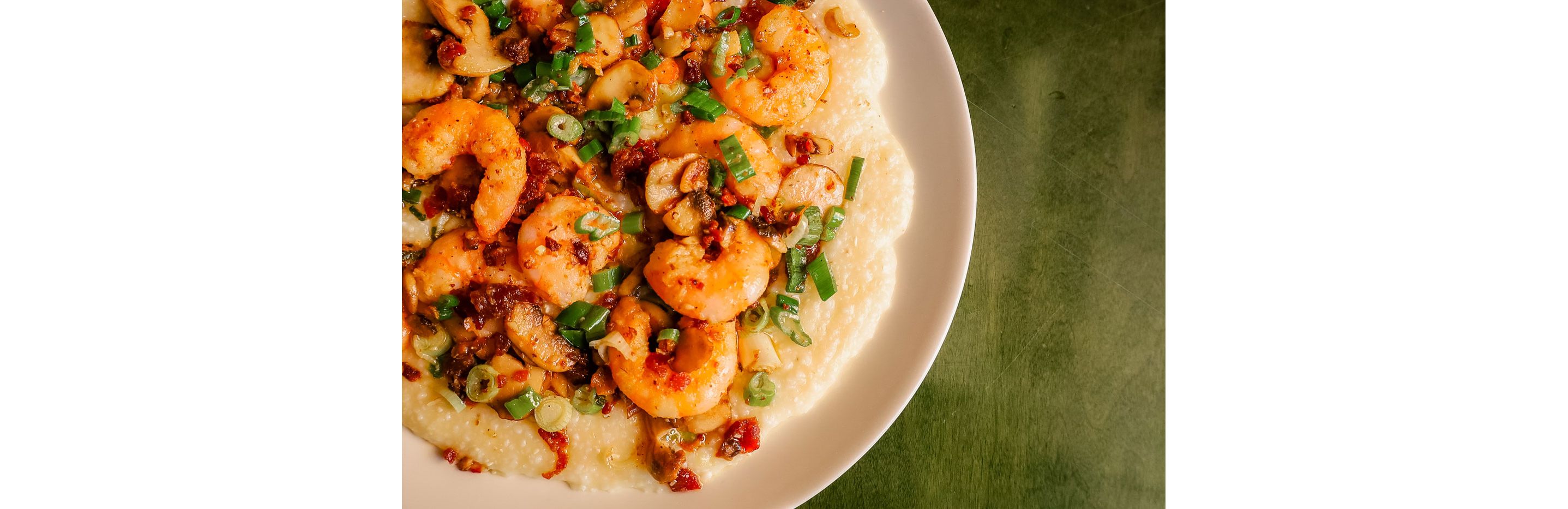 A closeup of a big, white bowl of shrimp and creamy grits.