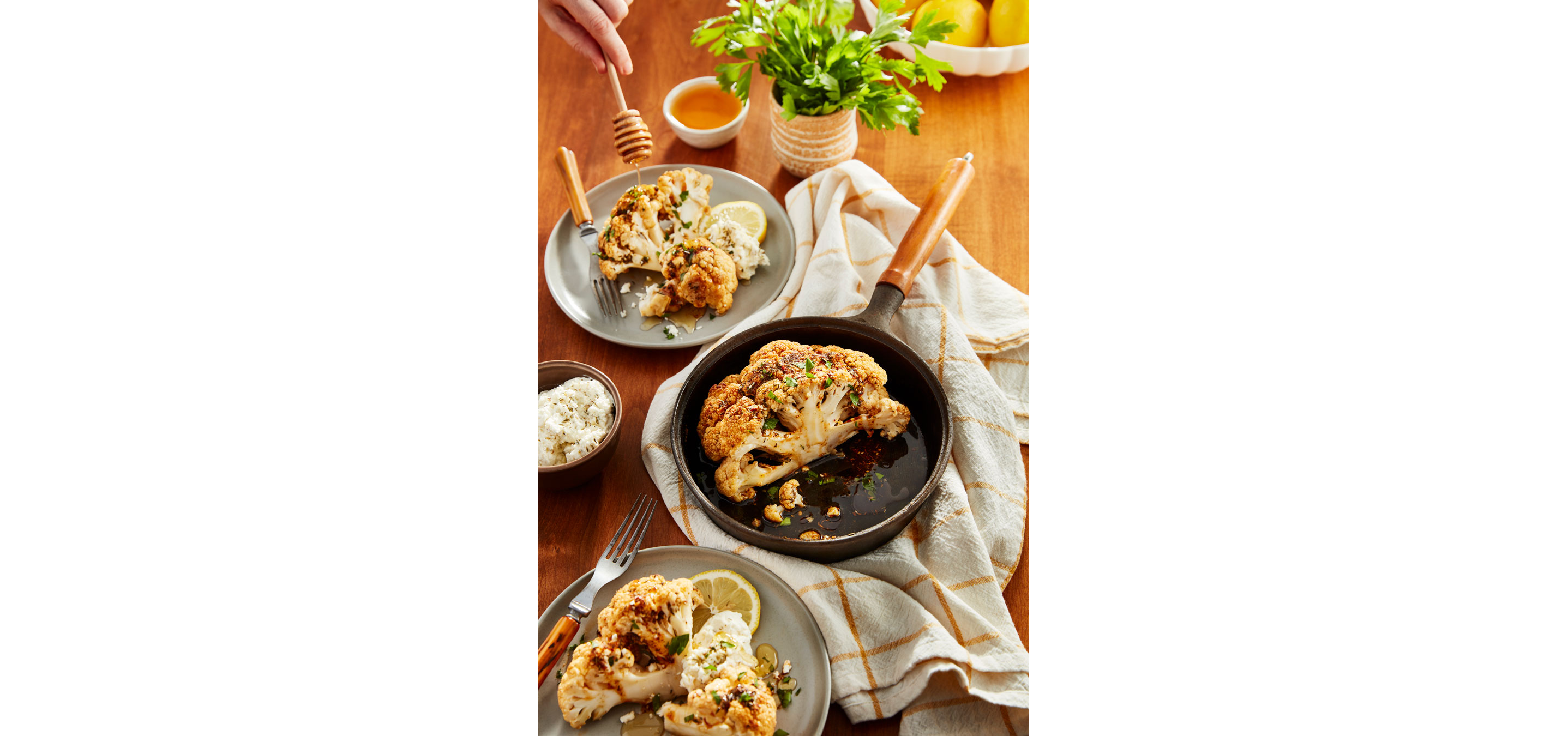 A skillet of roasted cauliflower surrounded by served plates.