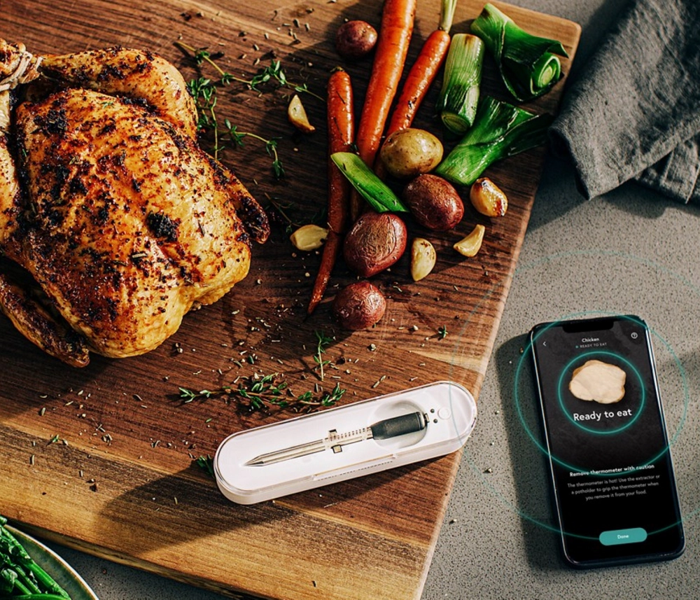 A cooked chicken and vegetables next to a smart thermometer.