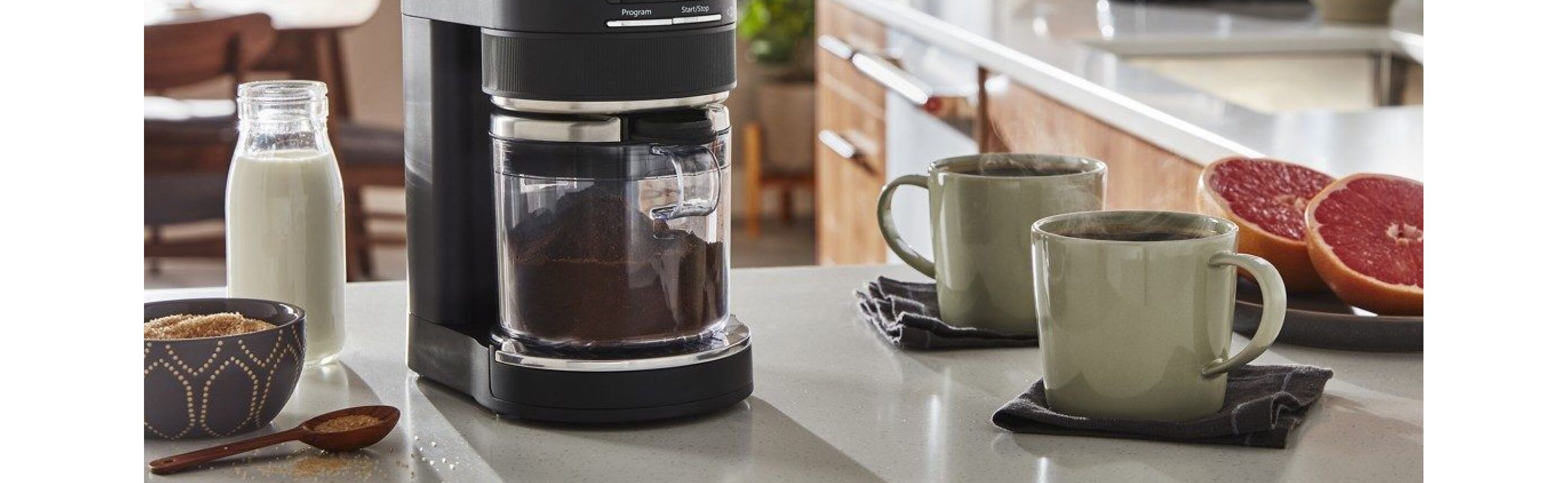 Best home coffee setup on countertop, including KitchenAid® Burr Grinder surrounded by milk, cinnamon, two cups of coffee and grapefruit.