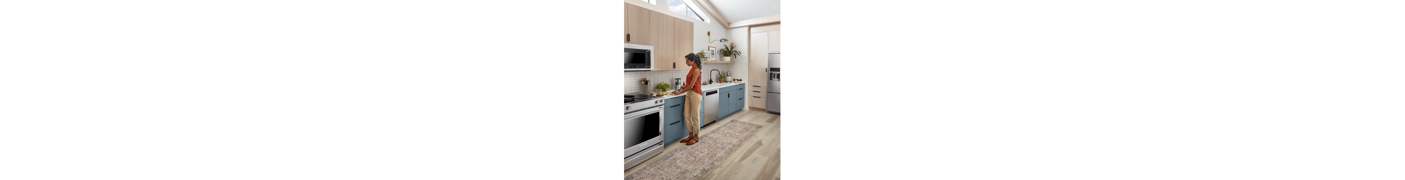A person in an L-shaped kitchen with blue and brown cabinetry
