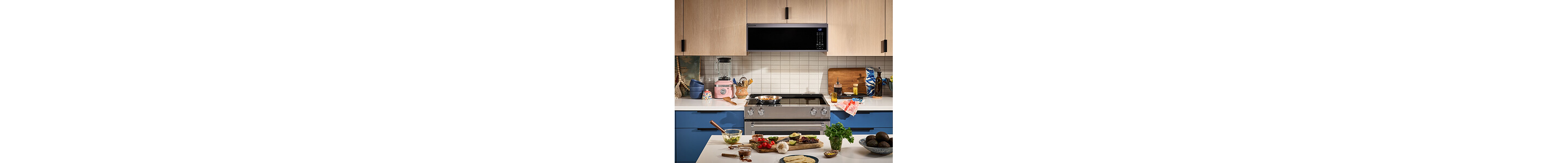A galley kitchen with blue lower cabinets and light wood upper cabinets against the wall side, and an island with white countertops on the other side
