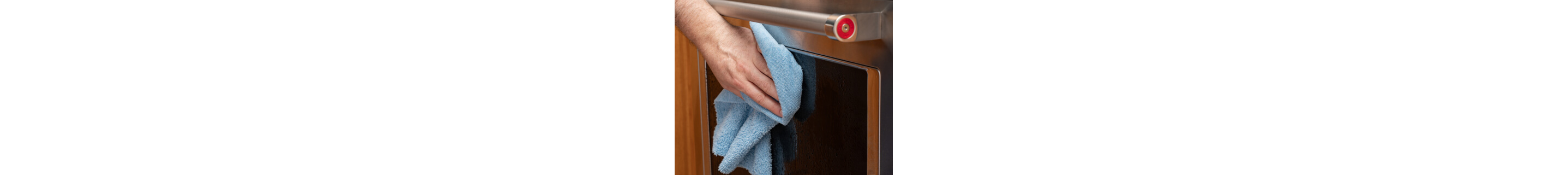 A close up image of oven door glass with a hand wiping it with a rag in the foreground