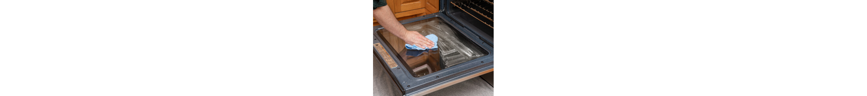 The inside of oven door glass with a hand wiping it down with a towel in the foreground