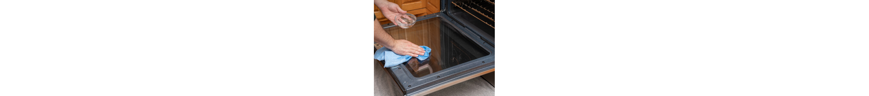 The inside of oven door glass with a hand wiping it down with a cloth treated with a vinegar or lemon mixture in the foreground