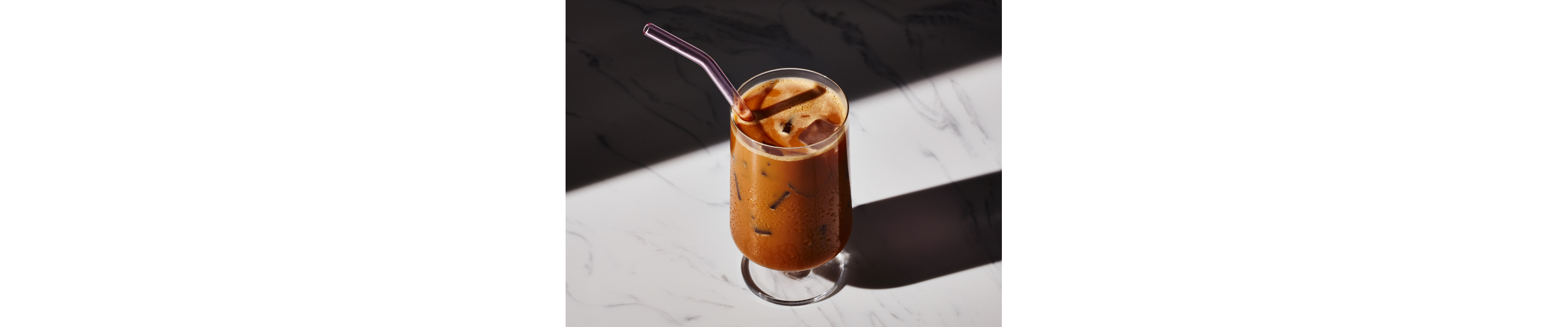 Glass of café con hielo with metal straw on granite countertop