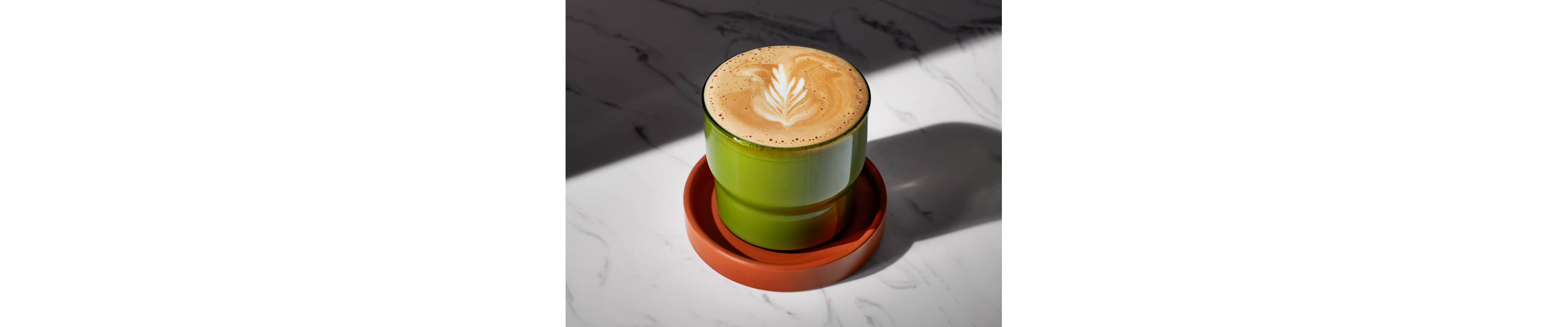 A piccolo latte in a green cup on a coaster