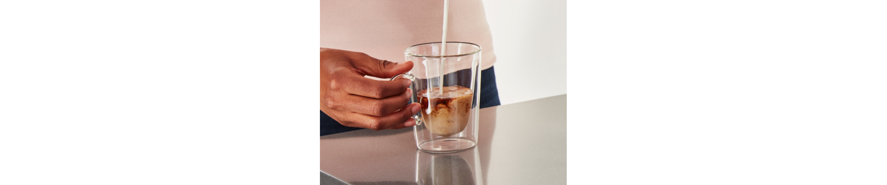 Person pouring steamed milk into a cortado in a glass mug