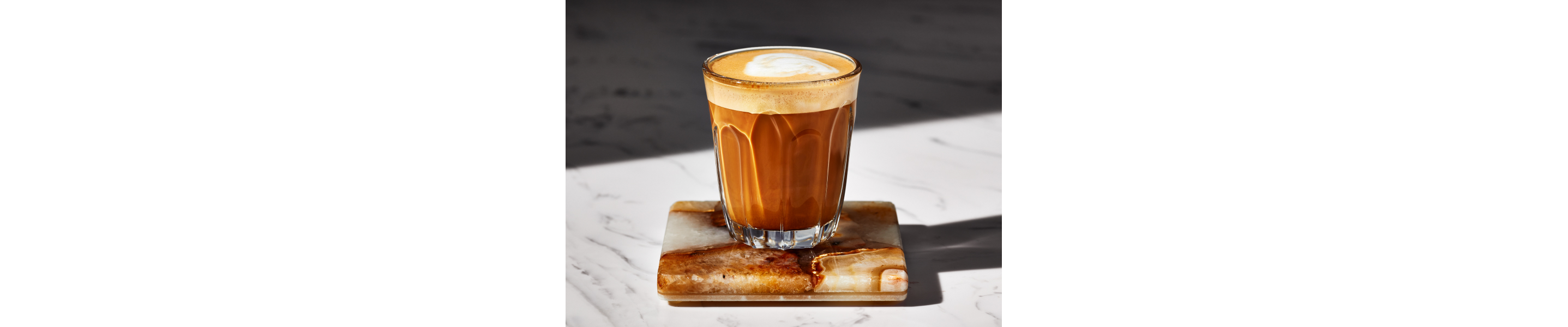 A breve in a glass cup on a dark granite coaster