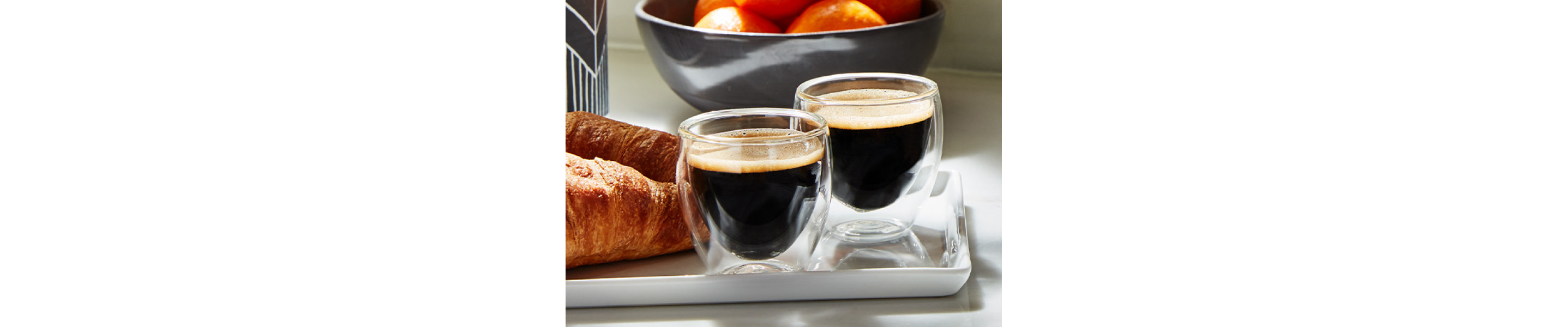 Two red eye espresso beverages on dish with croissants 
