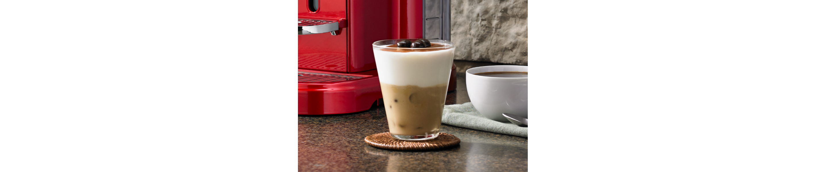 Latte macchiato on coaster near red espresso machine