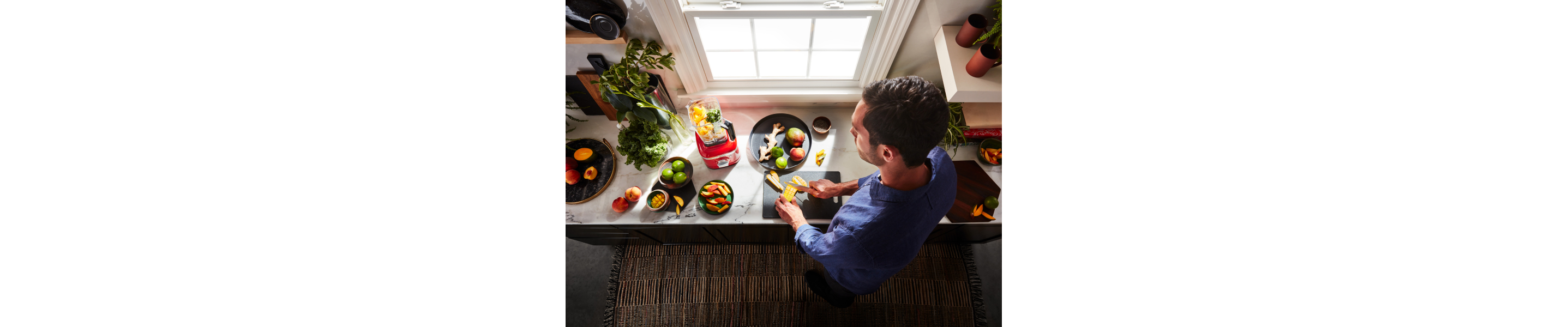 A person slicing fruit with a KitchenAid® blender nearby.
