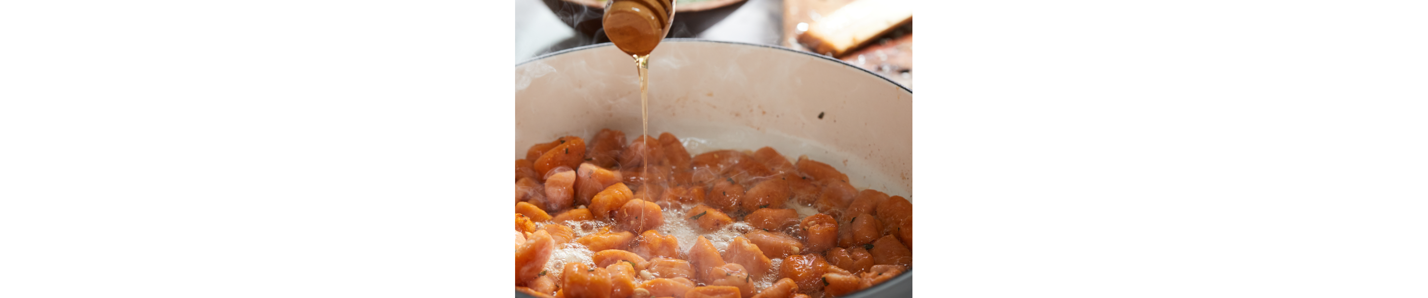 A wooden honey stick drizzling honey over sweet potato gnocchi sauteing on the stovetop.