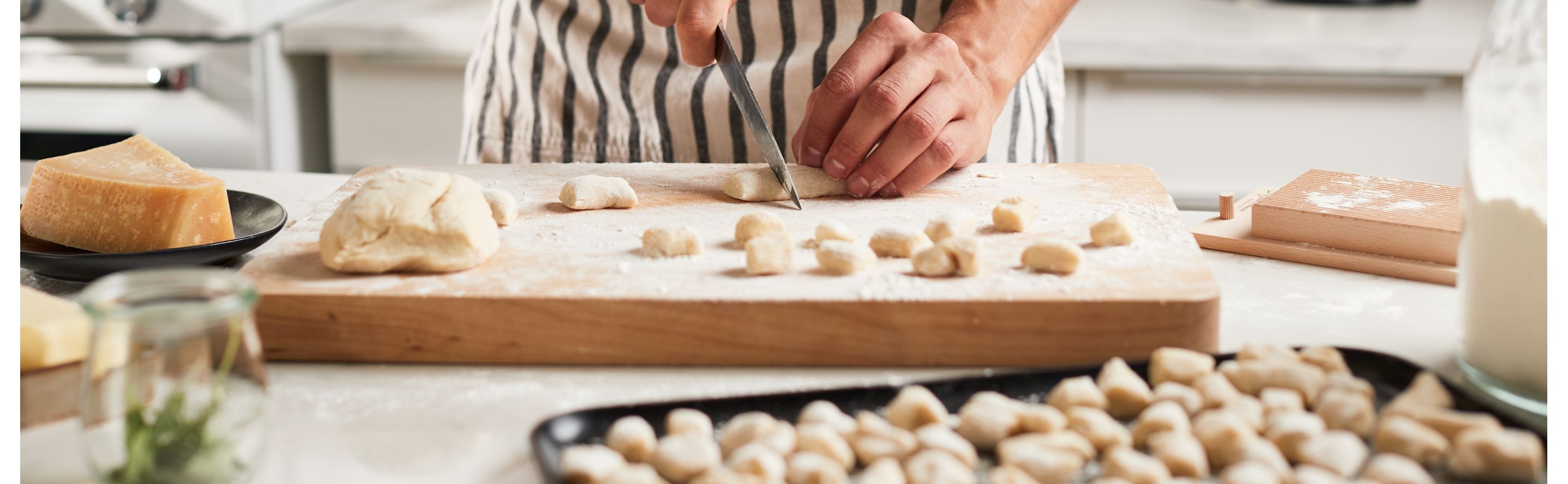 A man cutting pieces of potato gnocchi dough and placing them on a baking sheet in a modern kitchen. 