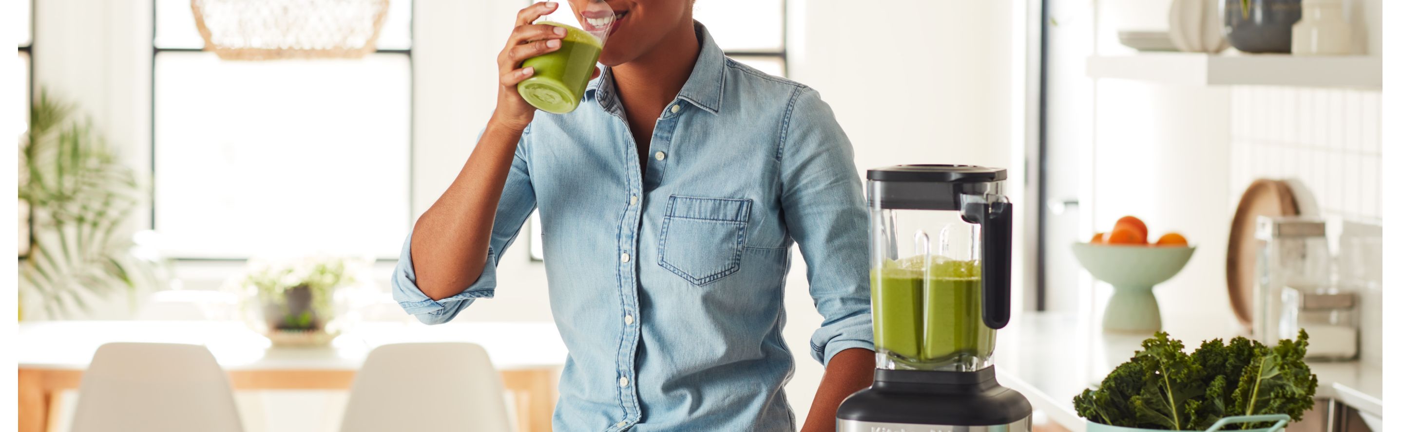 Person drinking green juice next to a KitchenAid® blender