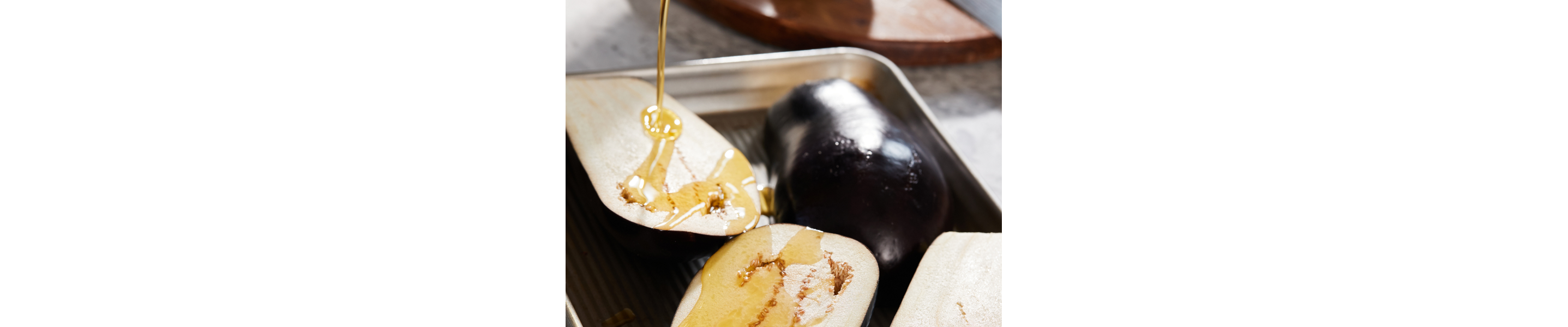 Olive oil drizzling on halved eggplants laying on baking sheet