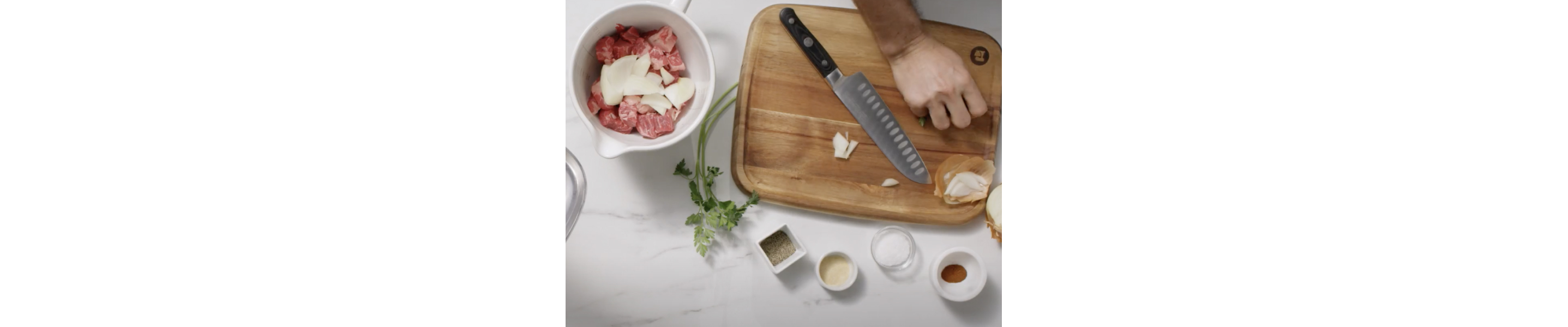 Person slicing onions and adding them to a bowl of raw meat
