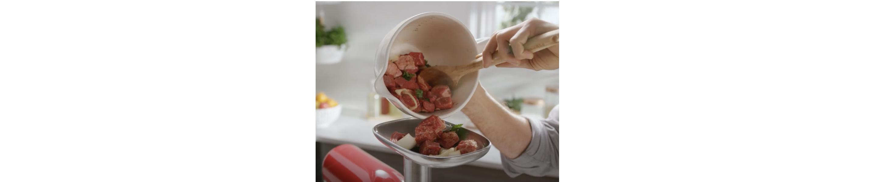 Person adding cubes of meat into a KitchenAid® Meat Grinder Attachment