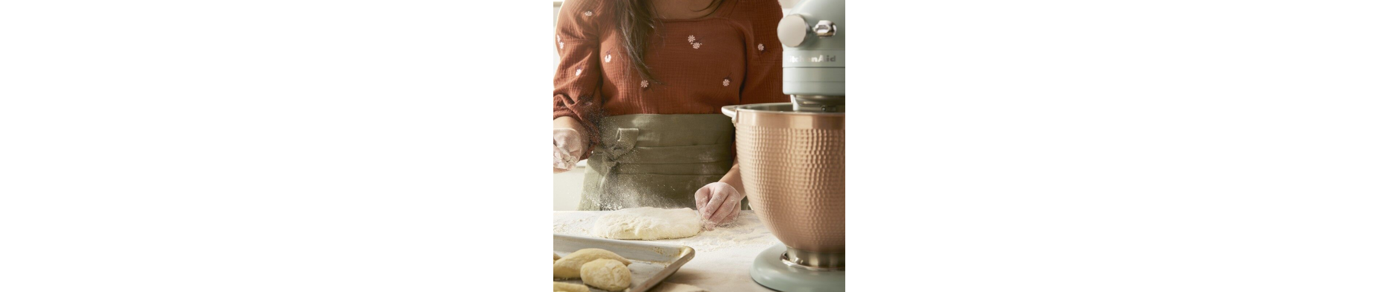 Person dusting bread dough with flour next to a KitchenAid® stand mixer