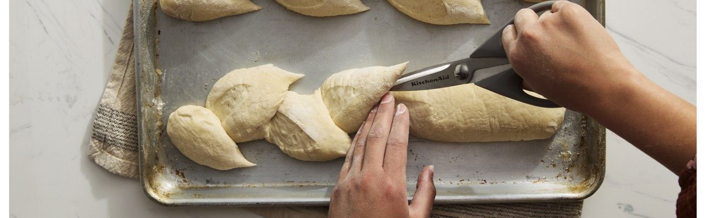 Person scoring bread on a baking sheet with kitchen scissors
