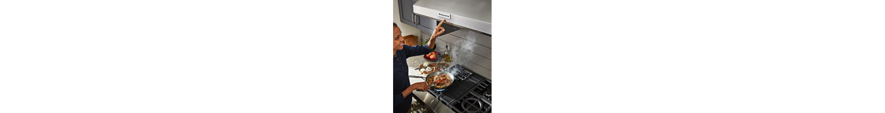 A person cooking on a KitchenAid® range, turning on the fan of a range hood