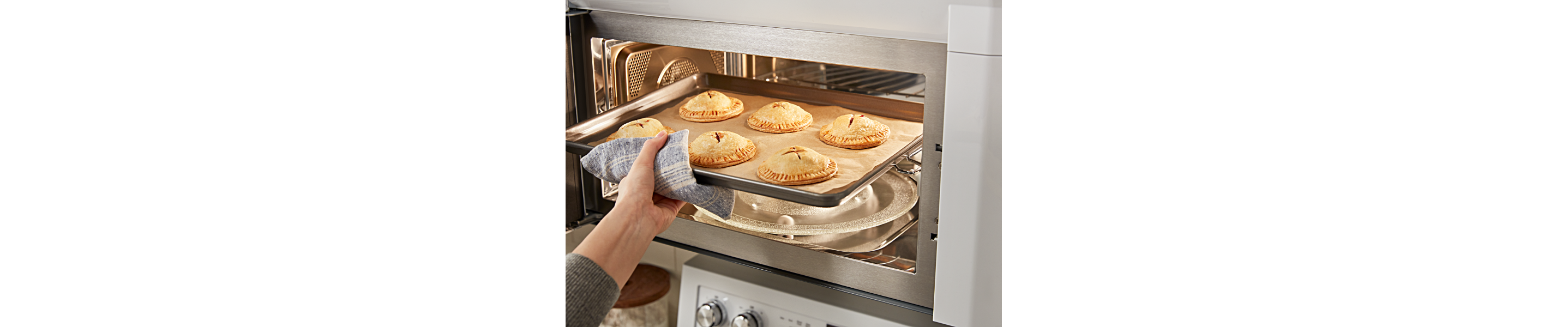 A person removing a sheet pan of baked pastries from a KitchenAid® microwave.