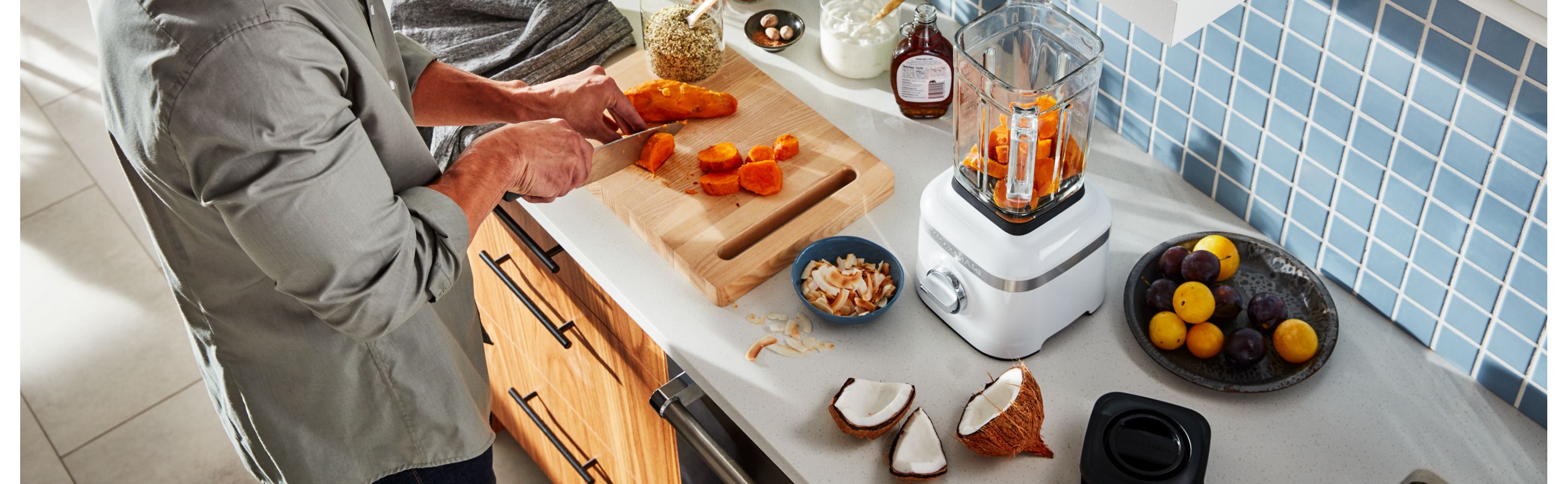 A man in a modern kitchen cutting vegetables to add to a KitchenAid® blender. 