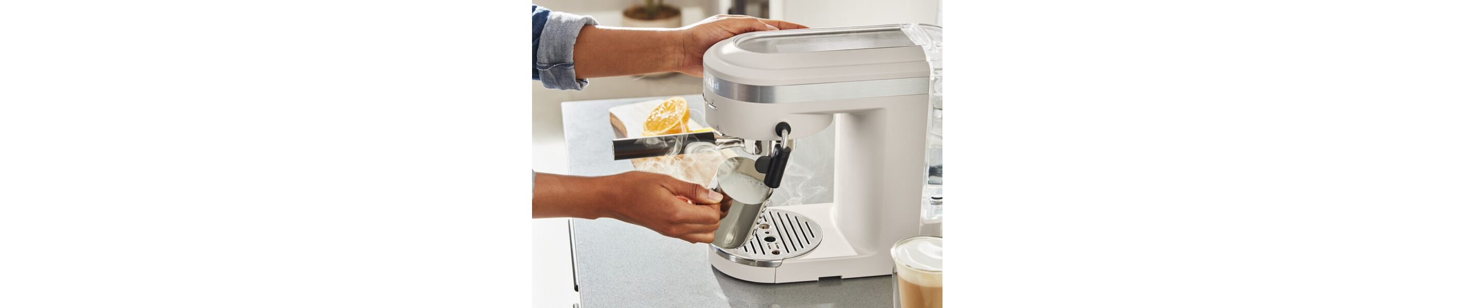 Person steaming milk in pitcher using a white espresso machine