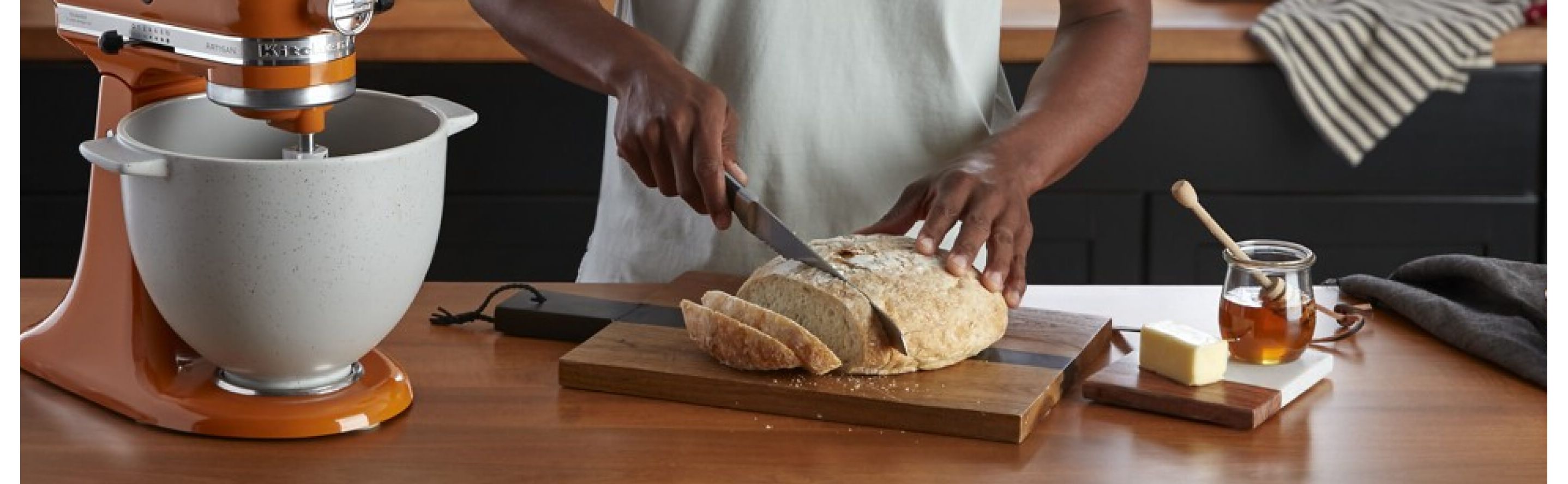  Person slicing a loaf of bread next to a KitchenAid® stand mixer