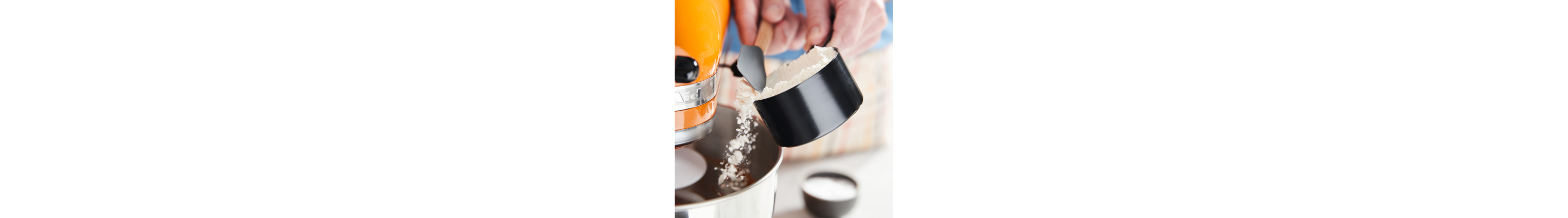 A person scraping flour into an orange KitchenAid® stand mixer bowl