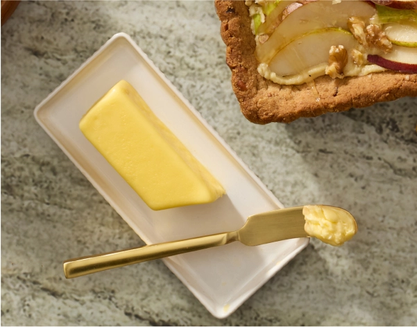 A stick of butter on a butter plate with a brass spreader