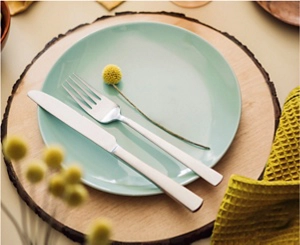 A tablesetting for one with a charcoal gray napkin, a glazed teal plate and decorative yellow flowers