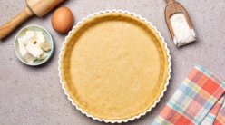 A tart crust and various baking implements and ingredients on a grey countertop.
