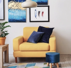 A rich yellow armchair with navy blue velvet pillows and a footstool
