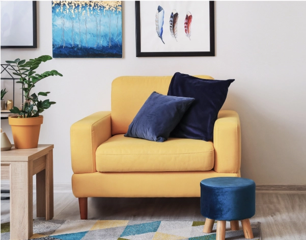 A rich yellow armchair with navy blue velvet pillows and a footstool