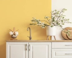 A kitchen sink set in a wooden countertop, with white cabinets and a bold yellow wall.