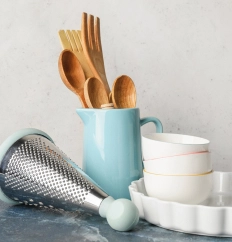 A grater and pitcher in robin's egg blue alongside wooden utensils and white dishes