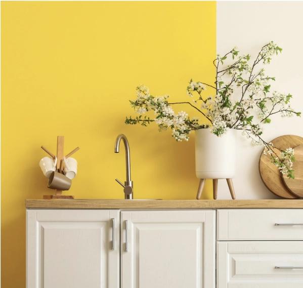A kitchen sink set in a wooden countertop, with white cabinets and a bold yellow wall.