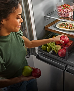 A person placing produce into a refrigerator drawer.