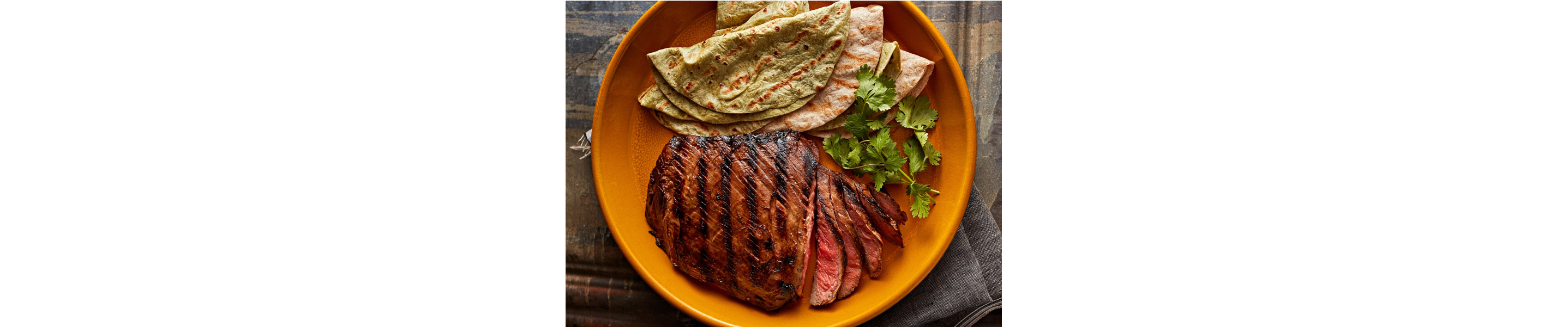 Grilled flat iron steak with green and yellow tortillas on the side