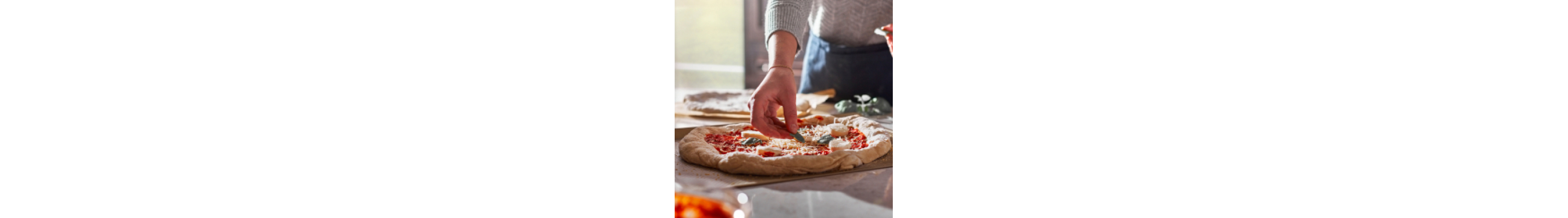 Person adding toppings to homemade pizza dough