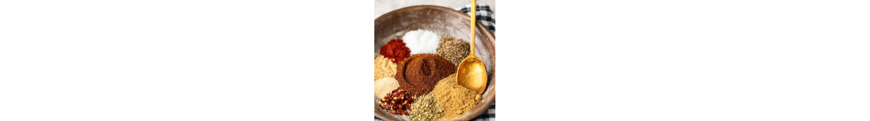 A variety of spices in a brown ceramic bowl with a wooden spoon