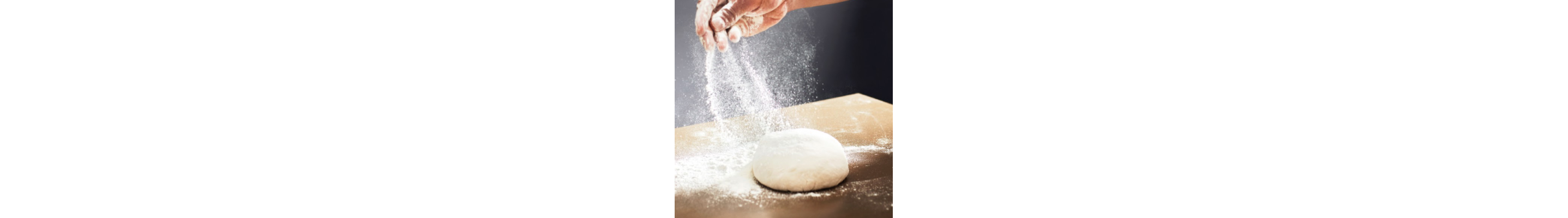 A person sprinkling flour onto a smooth kneaded dough ball on a wooden countertop