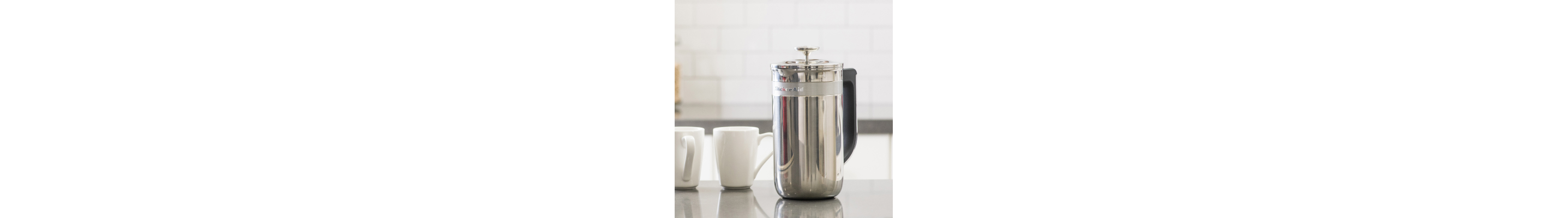 French press coffee maker next to two mugs