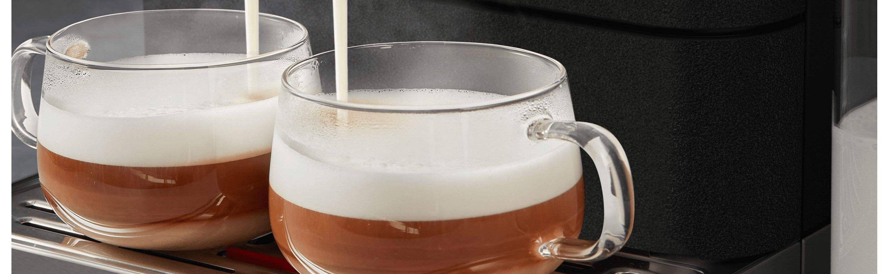 Glass mugs beneath an espresso machine being filled with frothed milk