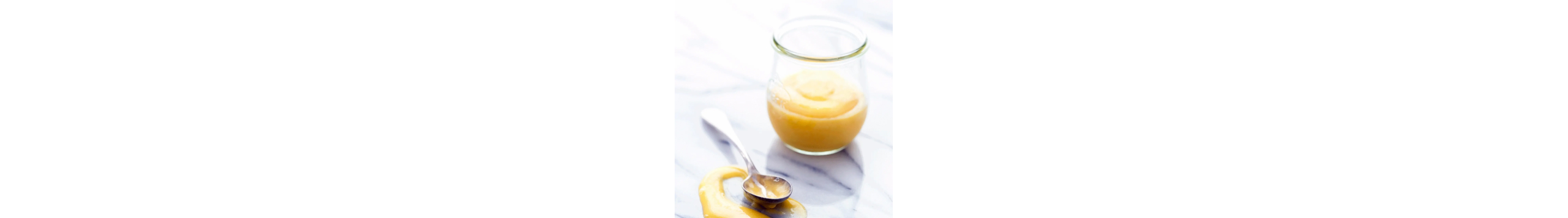 Mango curd in glass dish next to spoon on countertop 