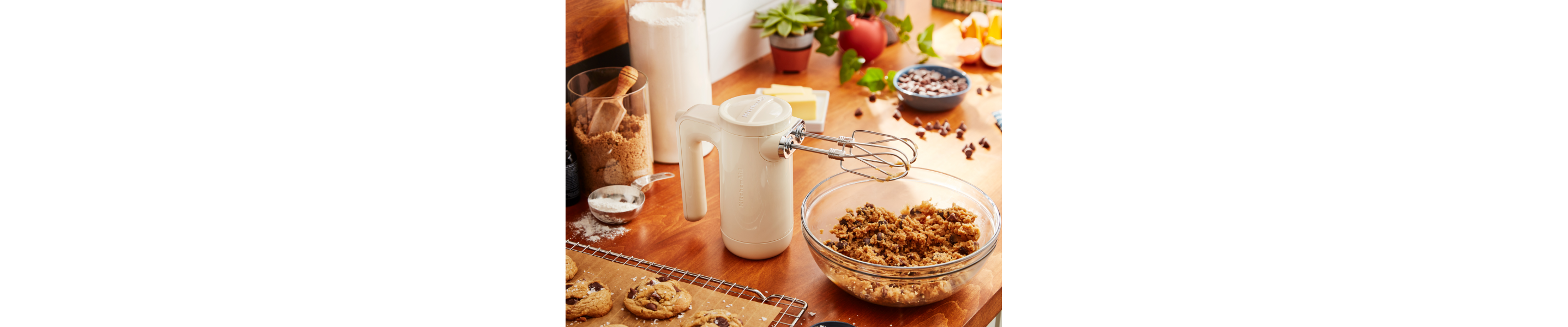 White KitchenAid® hand mixer resting on countertop above bowl of cookie dough