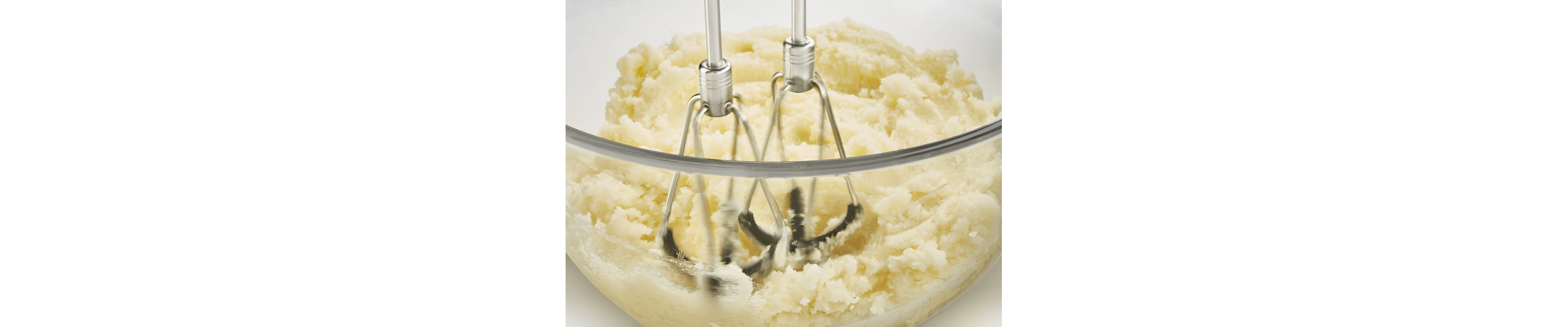Close up of flex edge beaters mixing mashed potatoes in glass bowl